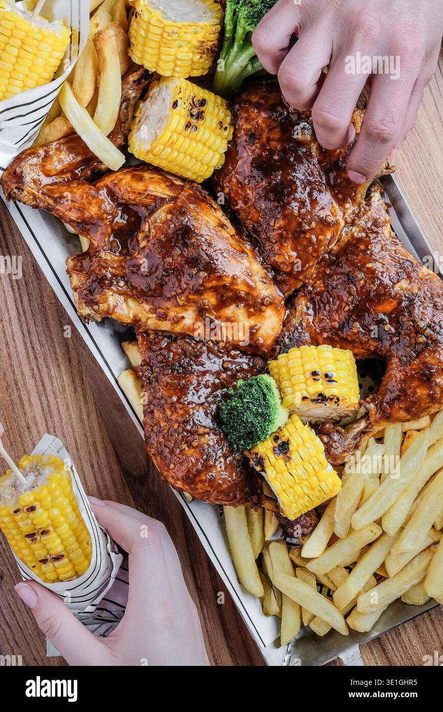 Ali succose con mais e patatine fritte. Pollo alla griglia con leccata di dita e glassa affumicata e contorni Foto Stock