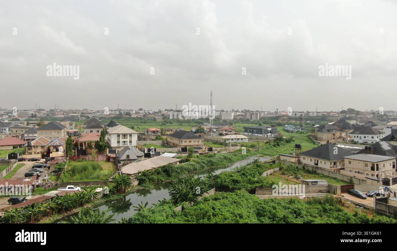 Una strada urbana strutturata a Lagos, Nigeria, che mostra veicoli in movimento e flusso di traffico regolare accanto a campi verdi paesaggistici, alberi ed edifici moderni. Foto Stock