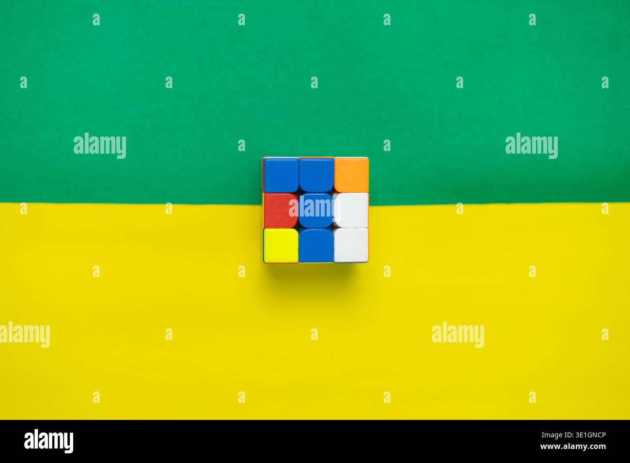 Un classico cubo di puzzle colorato con lati rossi, blu, gialli, arancioni e bianchi si appoggia su uno sfondo diviso verde e giallo. Simbolo IT Foto Stock