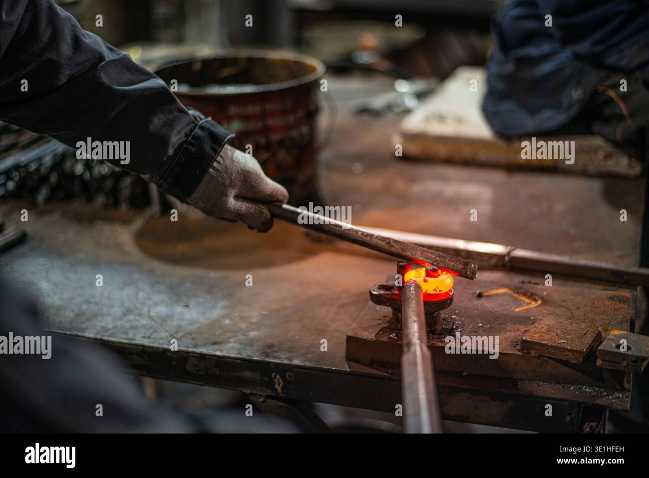 Nella bottega del fabbro, il fabbro sta livellando il metallo rosso-caldo con un martello. È in corso la preparazione di un pezzo di metallo caldo rosso con scala graduata per l'indurimento. Foto di alta qualità Foto Stock