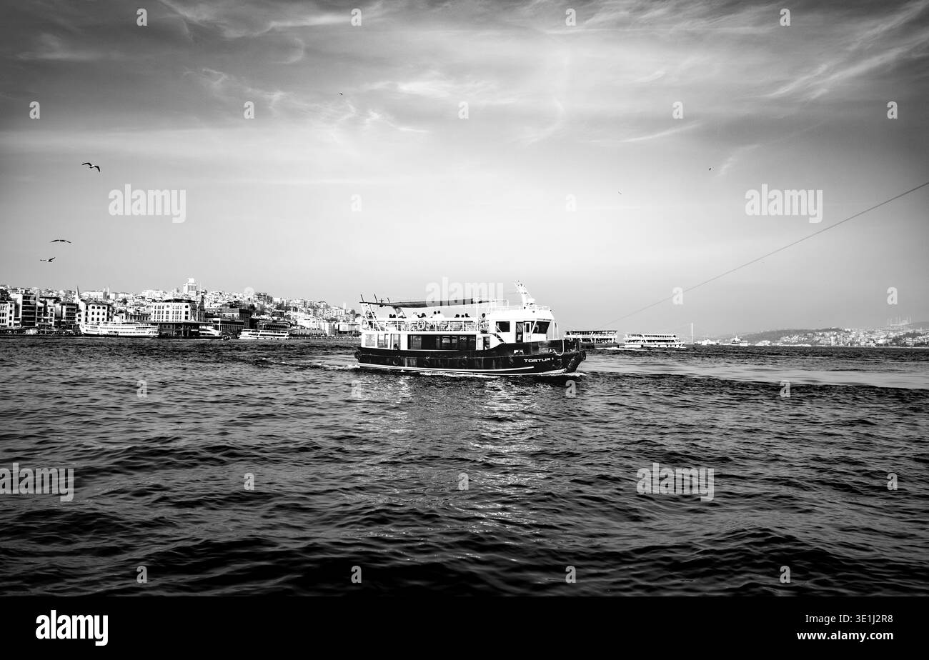 Un traghetto passeggeri naviga attraverso le acque instabili in questa spettacolare fotografia in bianco e nero. La costa urbana e il cielo nuvoloso creano una mariti soffice Foto Stock