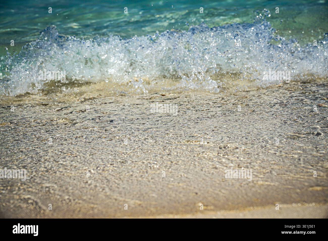 Onde oceaniche che si infrangono dolcemente sulla costa sabbiosa della spiaggia in acque poco profonde e cristalline, vista ravvicinata. Foto Stock