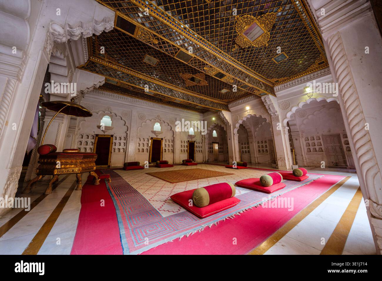 Le imbottiture rosse si trovano su un pavimento a motivi geometrici all'interno del Moti Mahal di Jodhpur, caratterizzato da un soffitto in foglia oro e pareti in gesso bianco lucido. Jodhpur Rajast Foto Stock