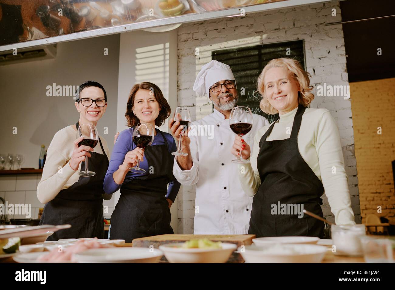 Diversi adulti di mezza età e chef che partecipano alla lezione di cucina per tostare il vino Foto Stock
