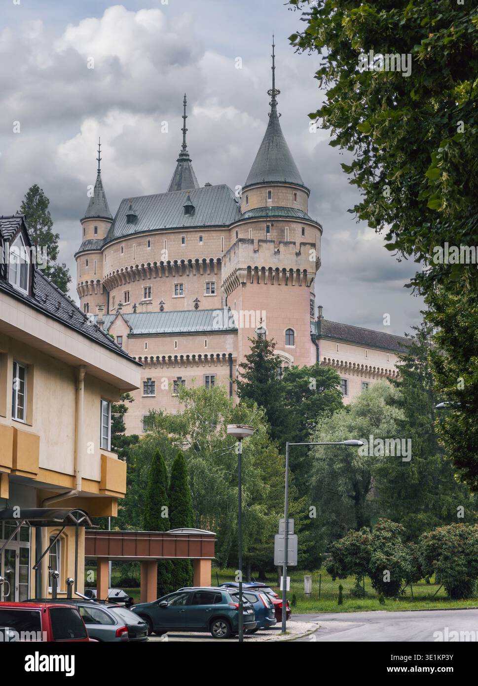 Vista più ravvicinata della città delle torri superiori del castello di Bojnice che si innalzano sopra edifici, alberi e auto parcheggiate nelle vicinanze a Bojnice, Slovacchia. Foto Stock