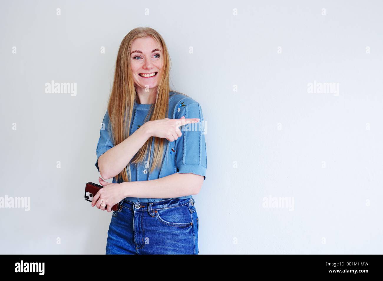 Giovane donna felice che indica uno sfondo vuoto. Promozione, idea e presentazione di marketing. Foto Stock