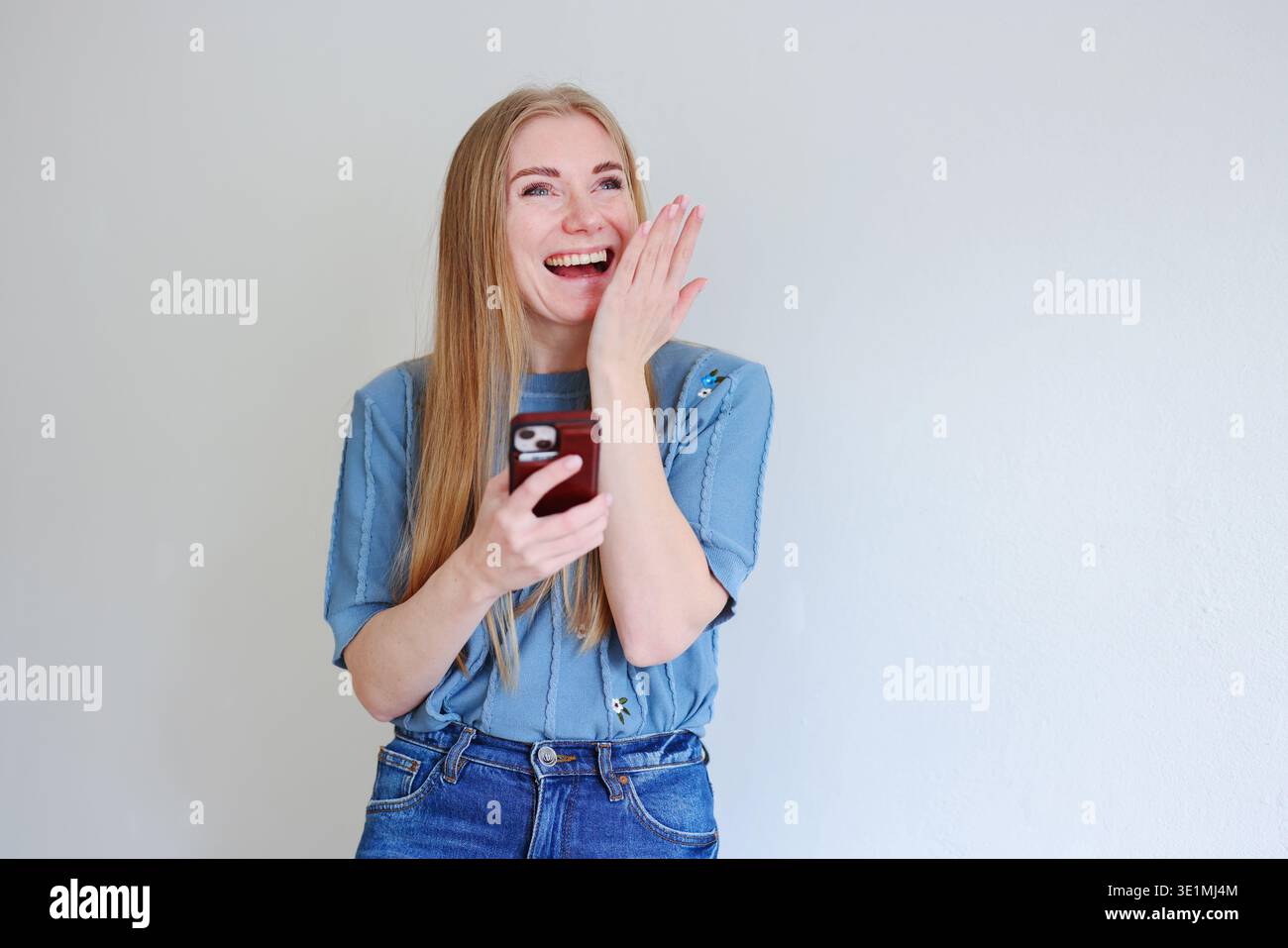 Giovane donna felice che ride mentre legge il messaggio sullo smartphone. Comunicazione mobile e moderno concetto di stile di vita digitale. Foto Stock