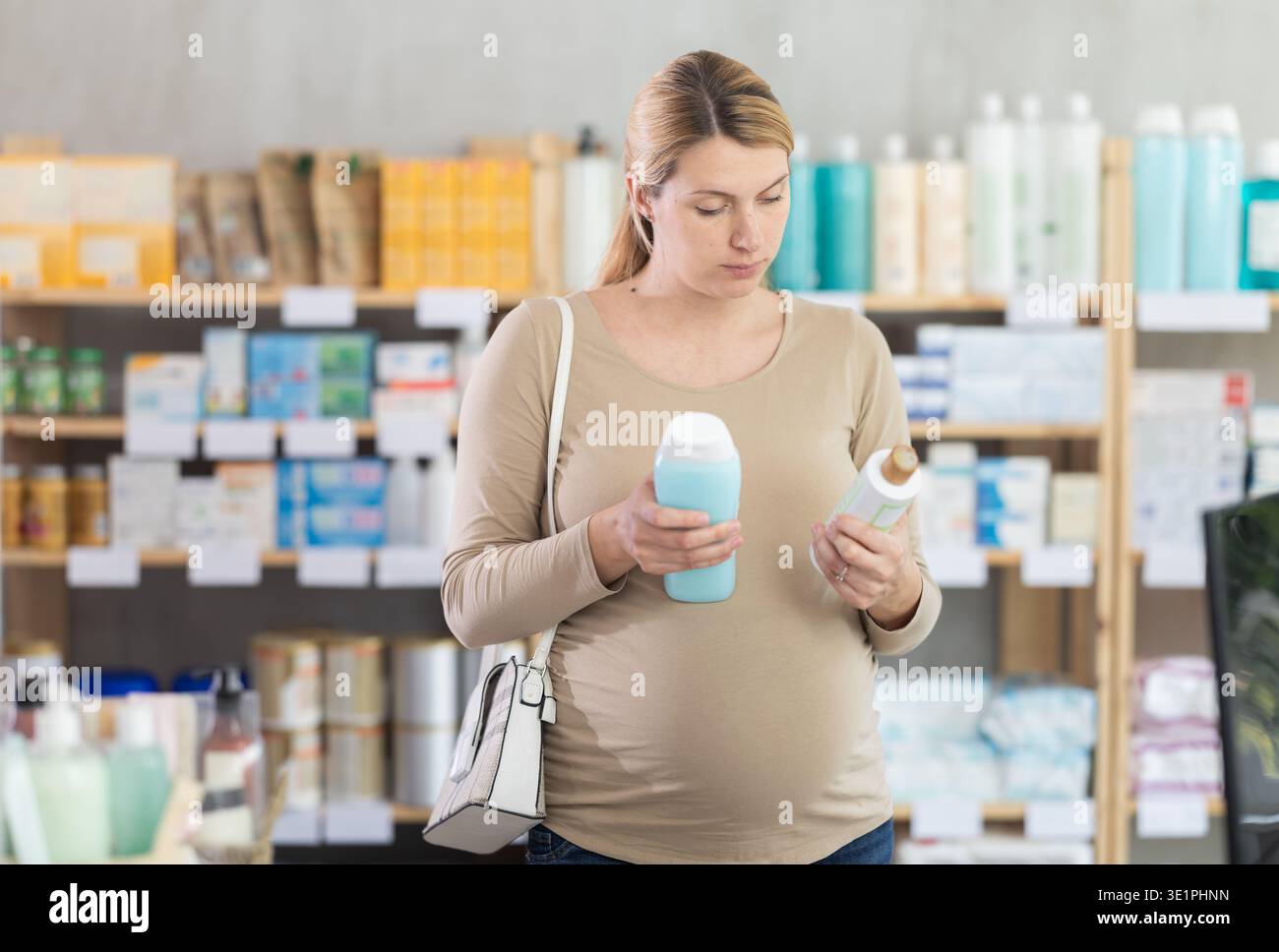 Donna incinta che sceglie lo shampoo in farmacia Foto Stock