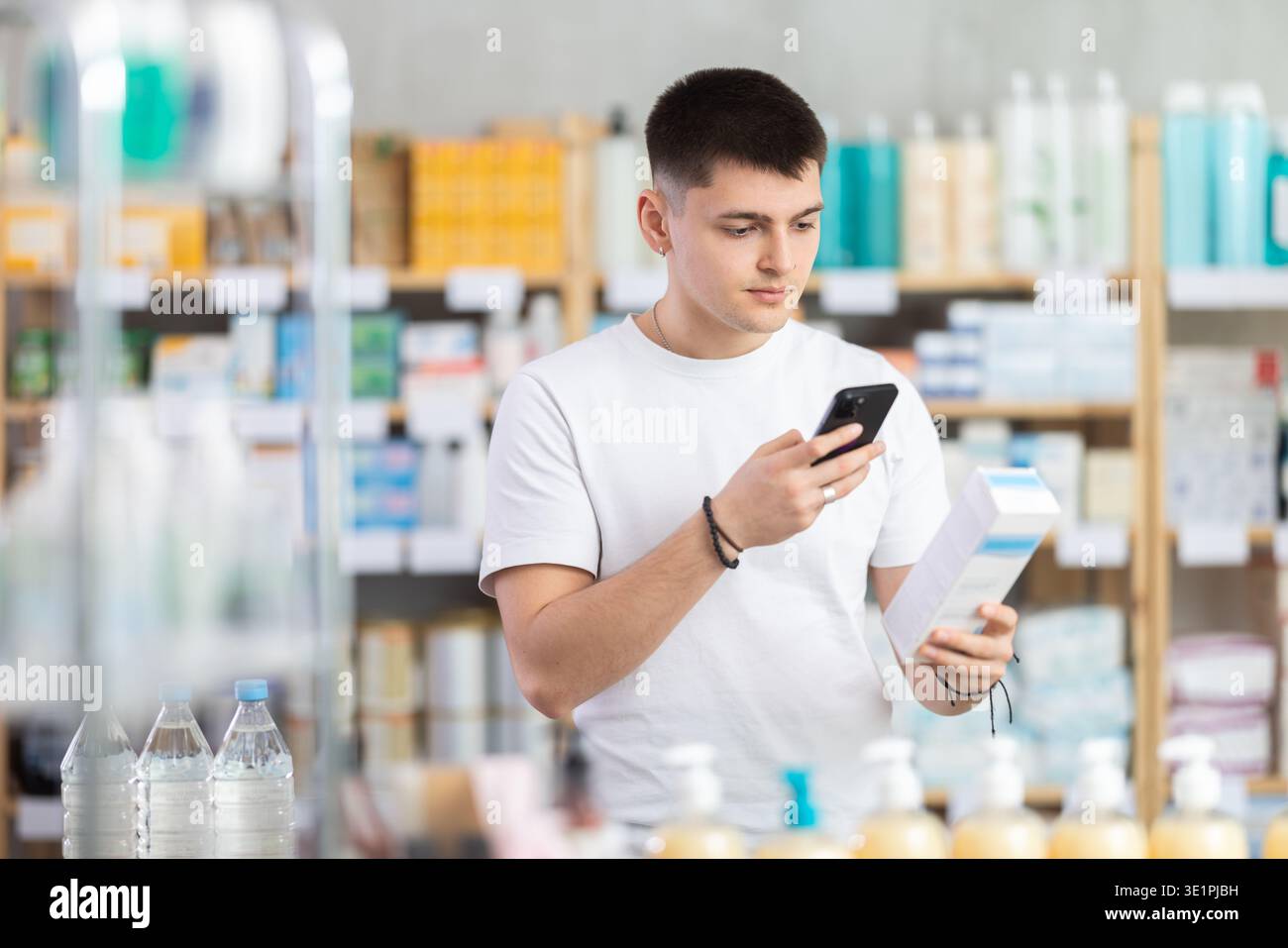 Attento giovane acquirente che esegue la scansione del codice qr per la scatola di unguento o gel in farmacia Foto Stock