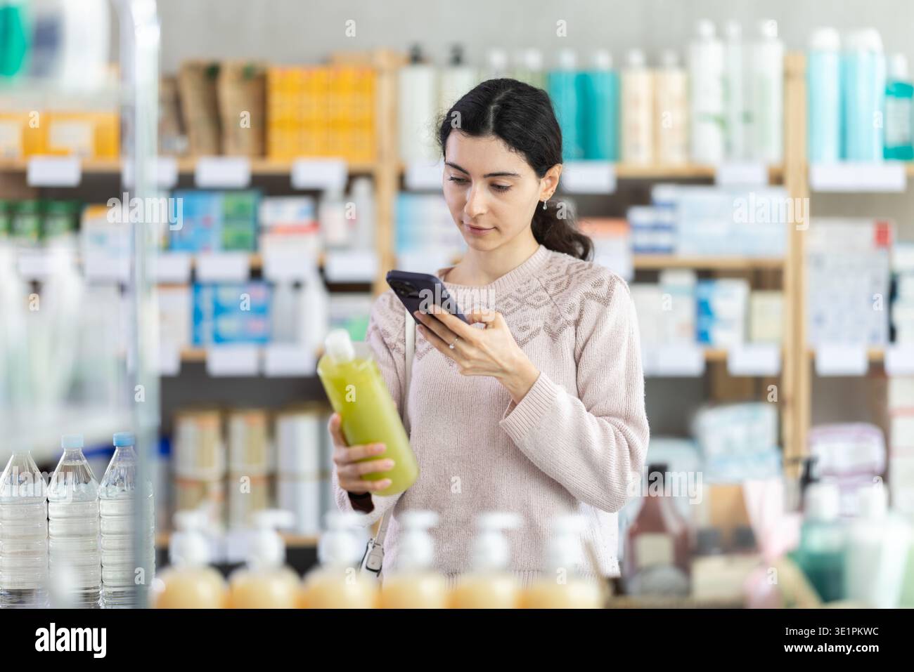 Ragazza in abiti autunnali scansione codice su shampoo medicinale per controllare la data di scadenza Foto Stock