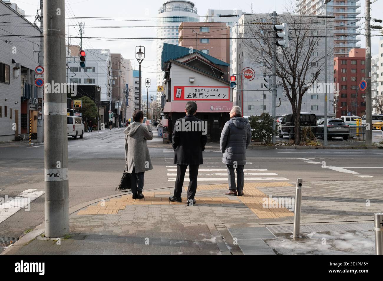 Tre persone aspettano in un incrocio della città di fronte a un negozio di ramen in Giappone Foto Stock