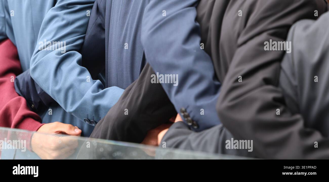 Uomini, giovani o ragazzi vestiti da dietro con abiti formali che mostrano armi legate in una dimostrazione di forza, unità e solidarietà. Foto Stock