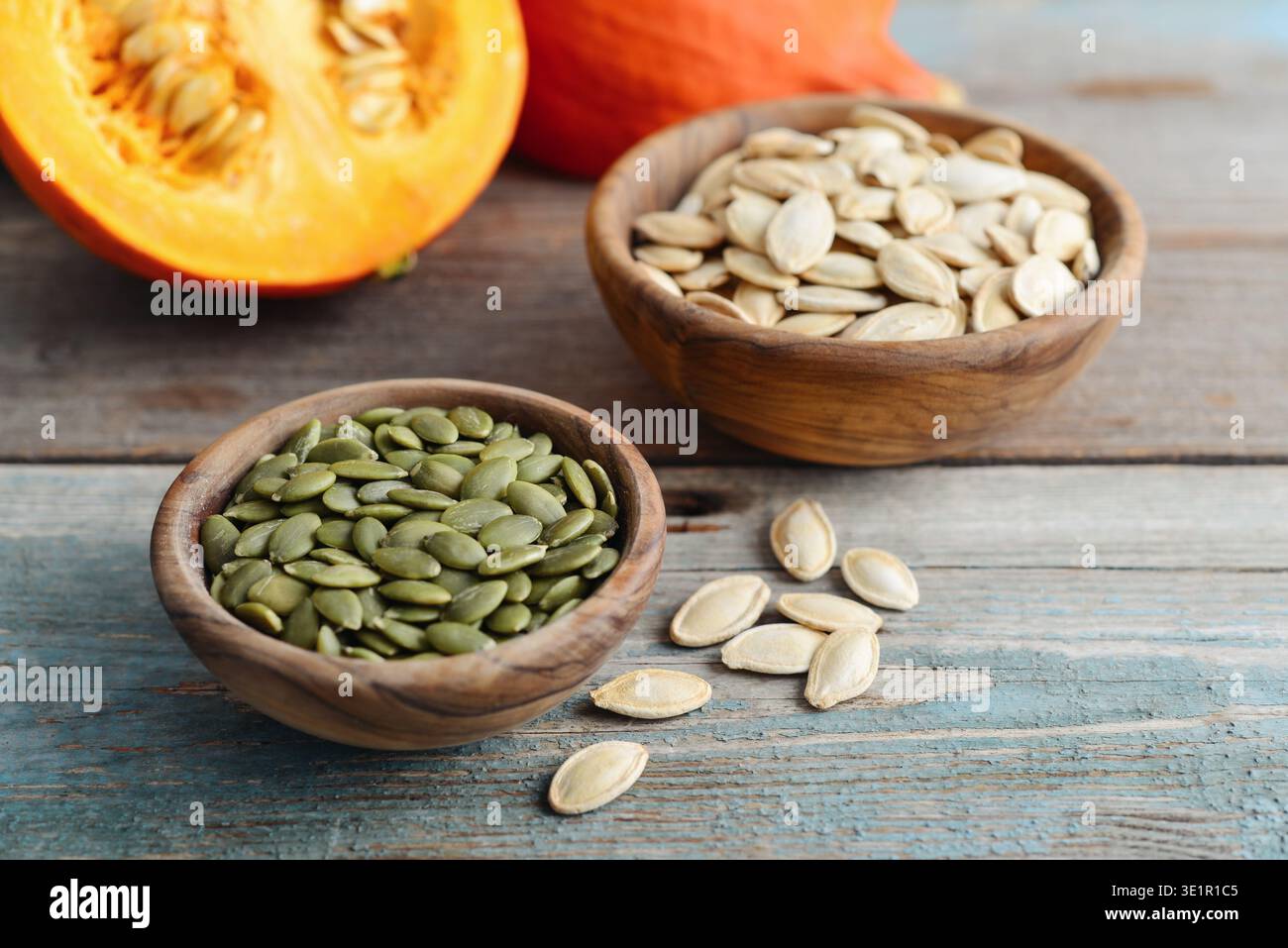 Zucche fresche e semi di zucca sbucciati e non sbucciati in ciotole di legno su un tavolo di legno, primo piano Foto Stock