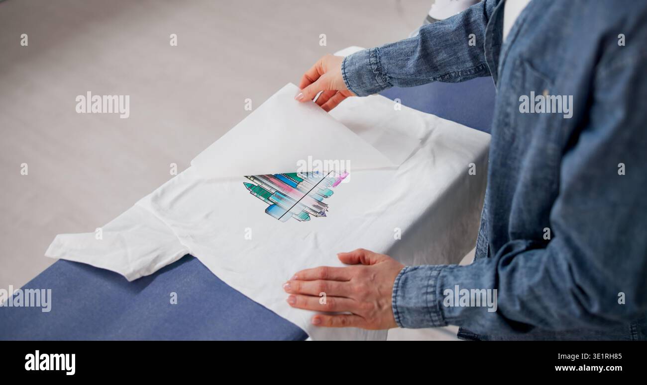 Donna che applica un design personalizzato a trasferimento di calore su una T-shirt con Iron at Home Foto Stock