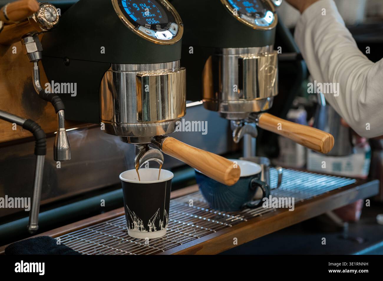 Macchina espresso che distribuisce il caffè in due tazze, una nera e una blu, con la mano del barista visibile in un bar Foto Stock