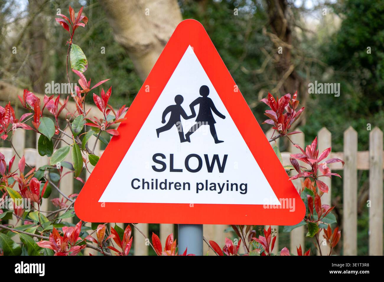 Segnaletica stradale triangolare britannica con bordo rosso, con una silhouette nera di due bambini e testo bambini LENTI che giocano, Regno Unito Foto Stock
