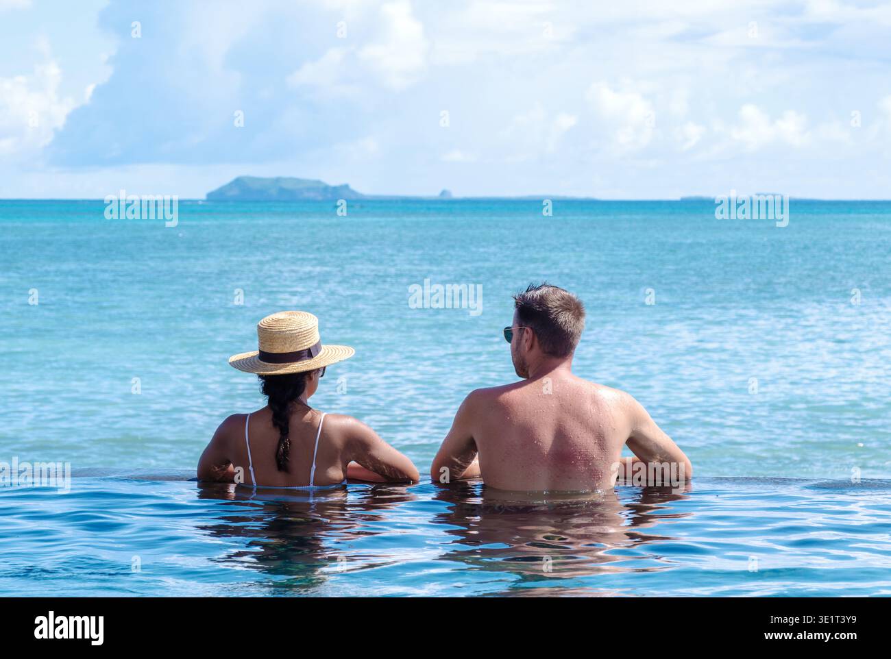 Due persone godono di un momento sereno al bordo di una splendida piscina a sfioro che si affaccia sull'oceano turchese mozzafiato di Mauritius. Foto Stock