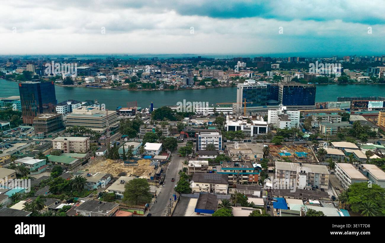 Veduta aerea degli edifici alti in mezzo alla distesa urbana, con la Laguna di Lagos che riflette il cielo coperto, Lagos, Lagos, Nigeria. Foto Stock
