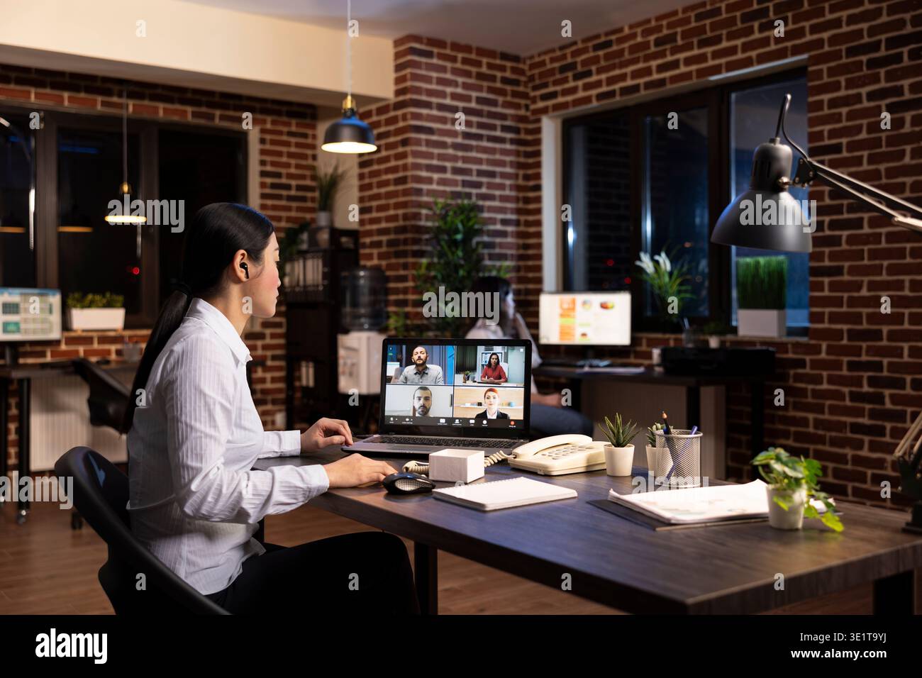 Una manager asiatica si impegna in una riunione virtuale con il suo team, condividendo idee di strategia aziendale durante una videoconferenza. Il laptop mostra che si connette con i dipendenti remoti durante il turno di notte. Foto Stock