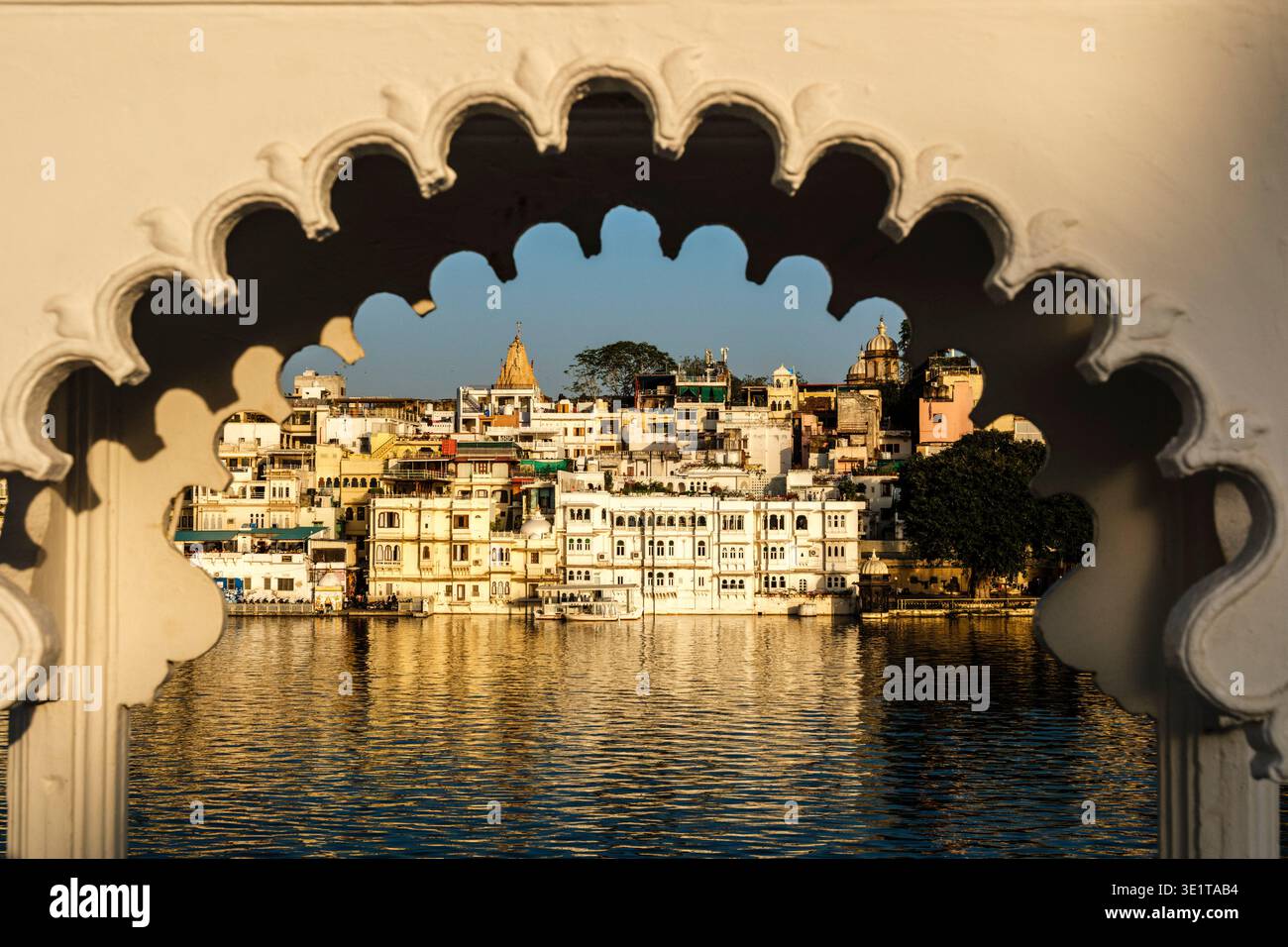 La calda luce del sole colpisce gli edifici sul lungomare di Udaipur, tra cui il Tempio Jagdish, incorniciato dall'arco smerlato ornato di una struttura in marmo. Foto Stock