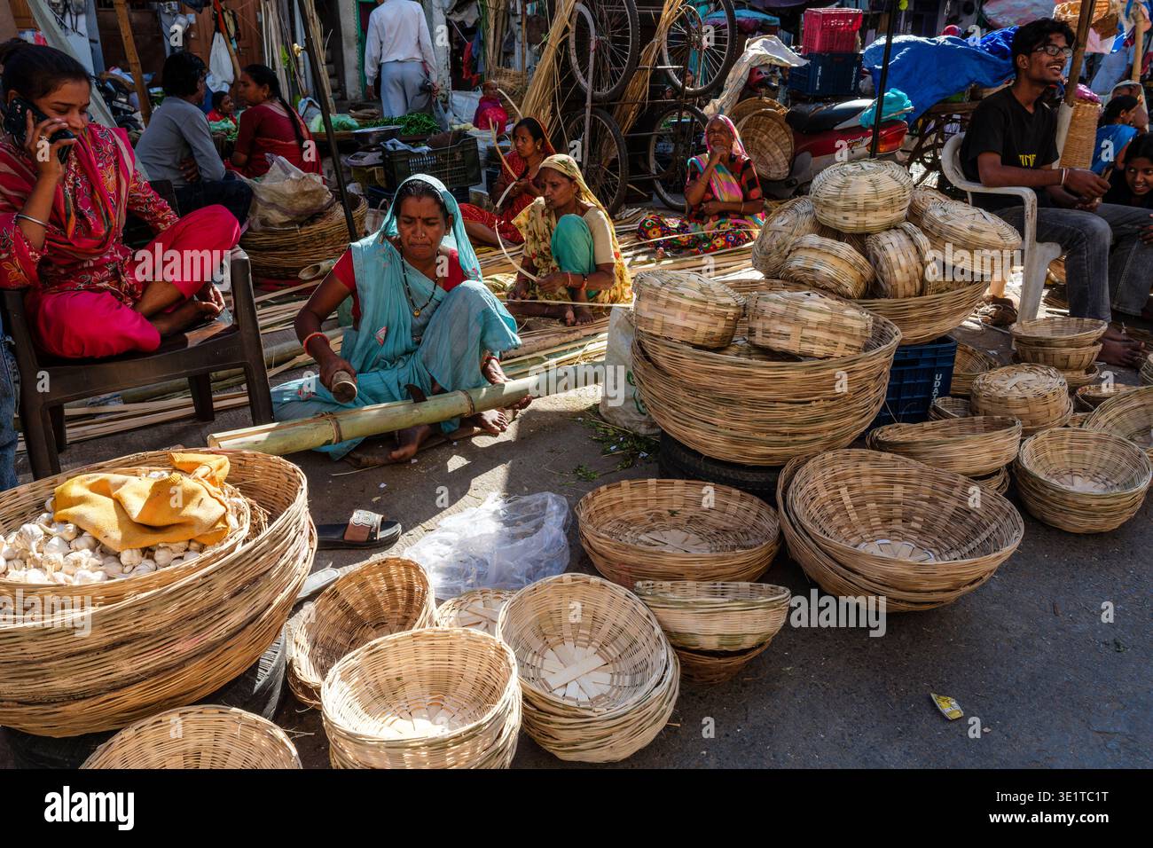 Diversi artigiani lavorano in una strada di Udaipur, lavorando bambù e cesti di tessitura tra una collezione di prodotti finiti e attività di mercato. Foto Stock