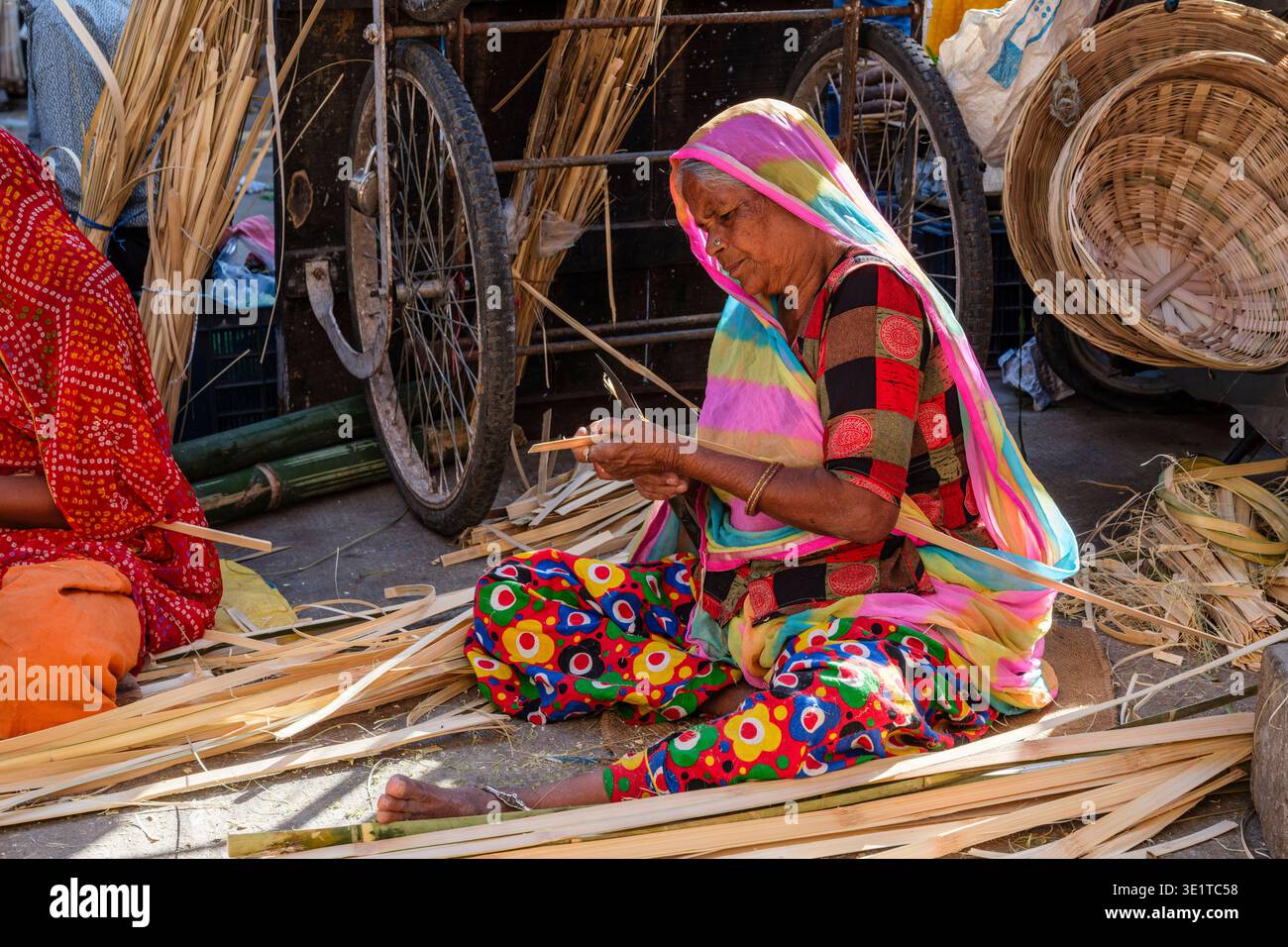 Una donna in un sari colorato rifinisce con cura le strisce di bambù mentre è seduta in una strada di Udaipur, circondata dagli strumenti della sua tessitura. Foto Stock