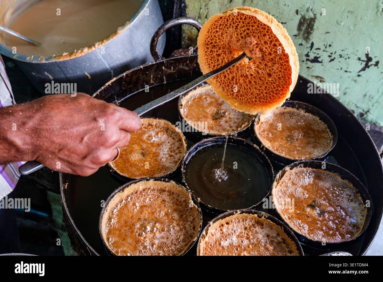 Un venditore di cibo di strada a Udaipur rimuove un dolce Ghevar dorato dall'olio bollente, mostrando la sua tradizionale consistenza porosa e la sua forma circolare. Foto Stock