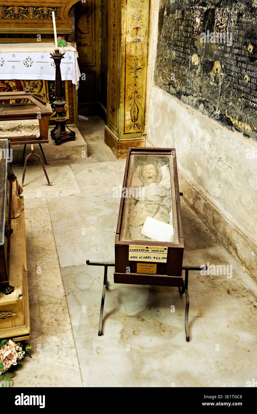 I visitatori osservano resti conservati in bare di vetro presso le Catacombe dei Cappuccini di Palermo, Sicilia, rivelando pratiche di sepoltura locali. Foto Stock