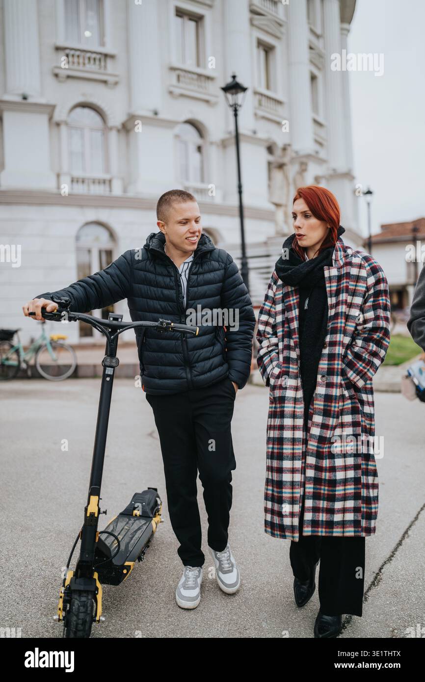 Due amici parlano accanto a uno scooter elettrico giallo su una strada della città di fronte a un grande edificio bianco Foto Stock