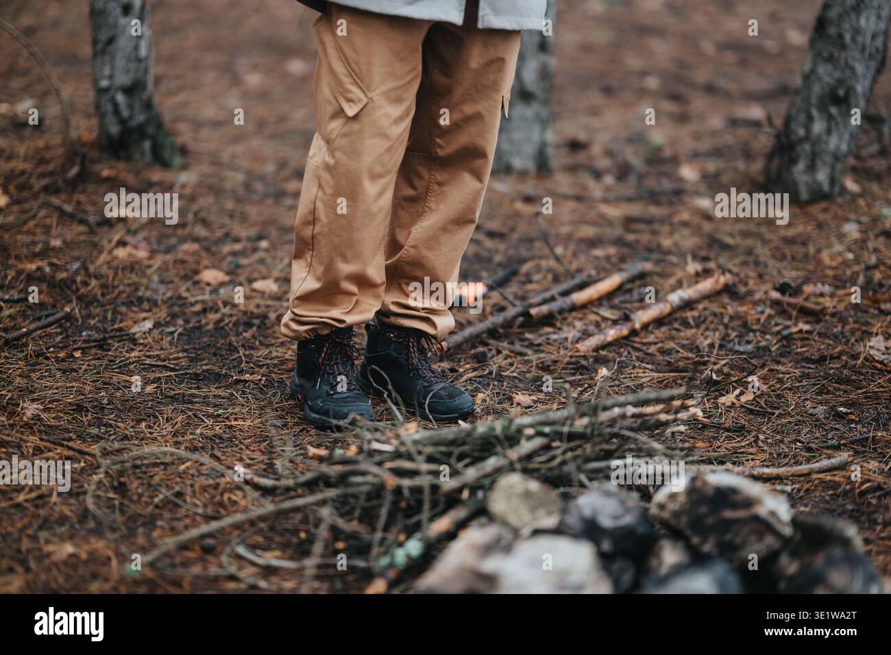 Amici in piedi accanto a un piccolo falò in una foresta di montagna con stivali da trekking e pantaloni abbronzati Foto Stock