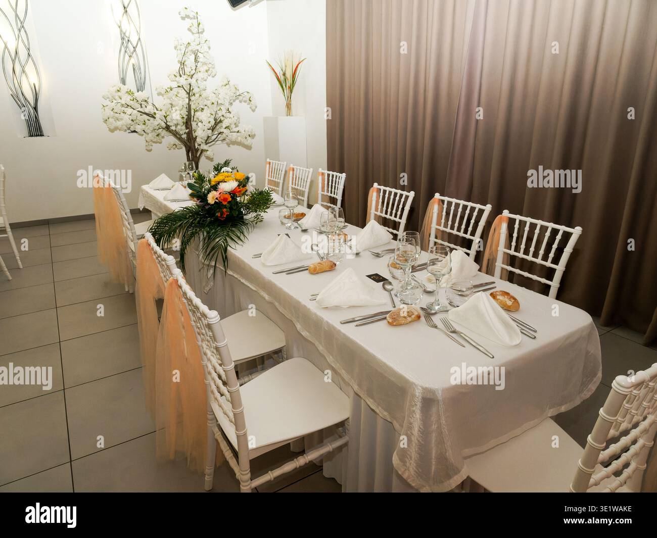 Elegante e lungo tavolo da banchetto preparato per un ricevimento di nozze con raffinati ambienti, centrotavola floreale e delicate tonalità decorative. Foto Stock