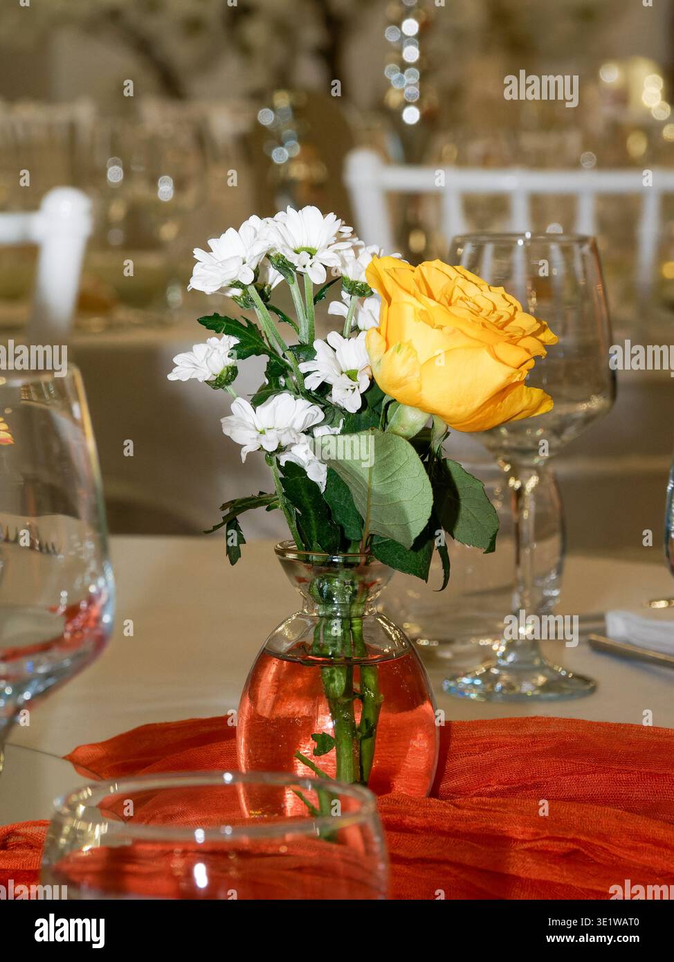 Elegante tavolo centrale con rosa gialla e fiori bianchi in vaso di vetro, perfetto per matrimoni, ricevimenti ed eventi raffinati. Foto Stock
