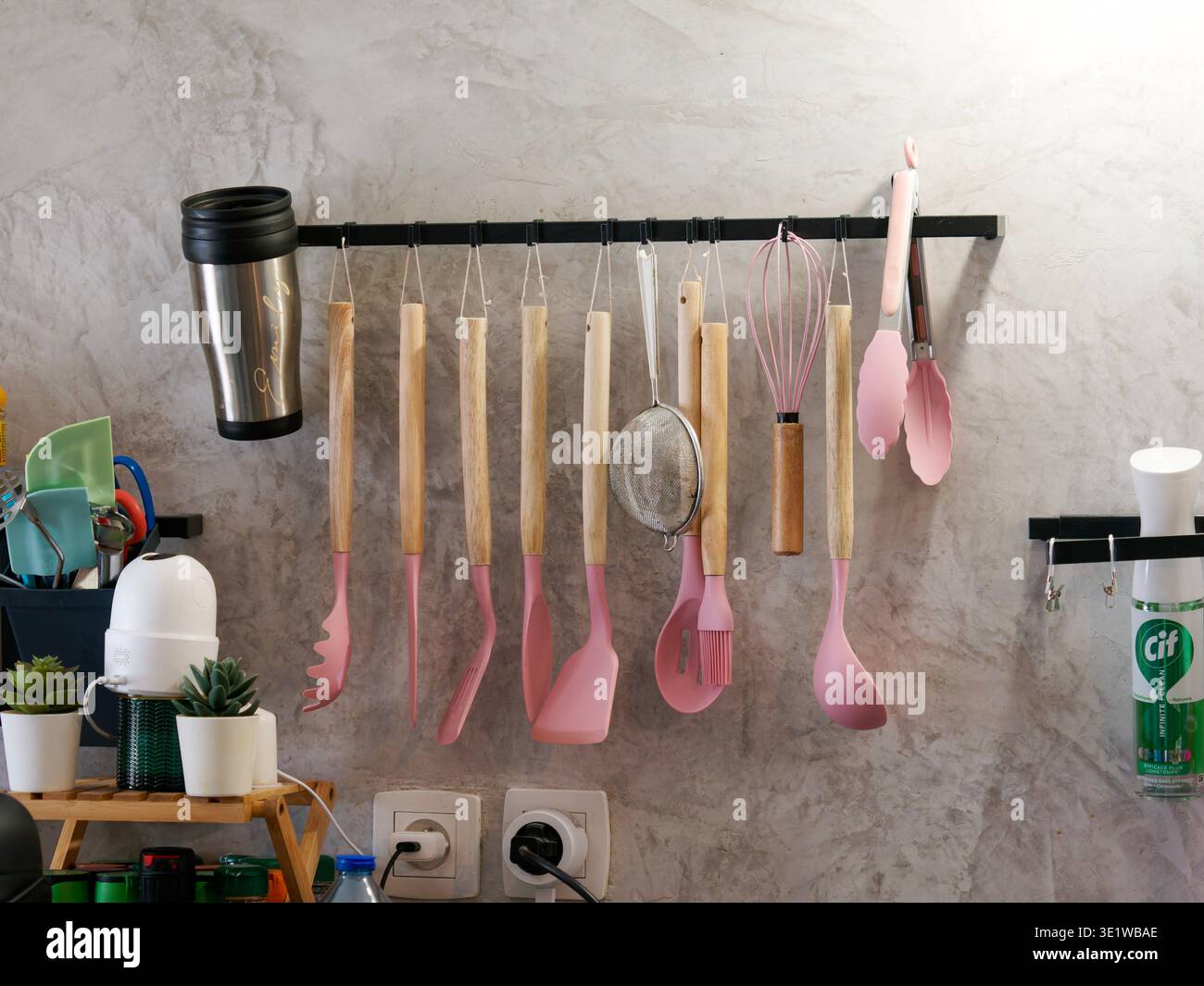 Utensili da cucina, tra cui spatole, frusta e mestolo disposti in modo ordinato su un rack montato a parete, che presenta un'organizzazione e una configurazione funzionale della cucina casalinga. Foto Stock