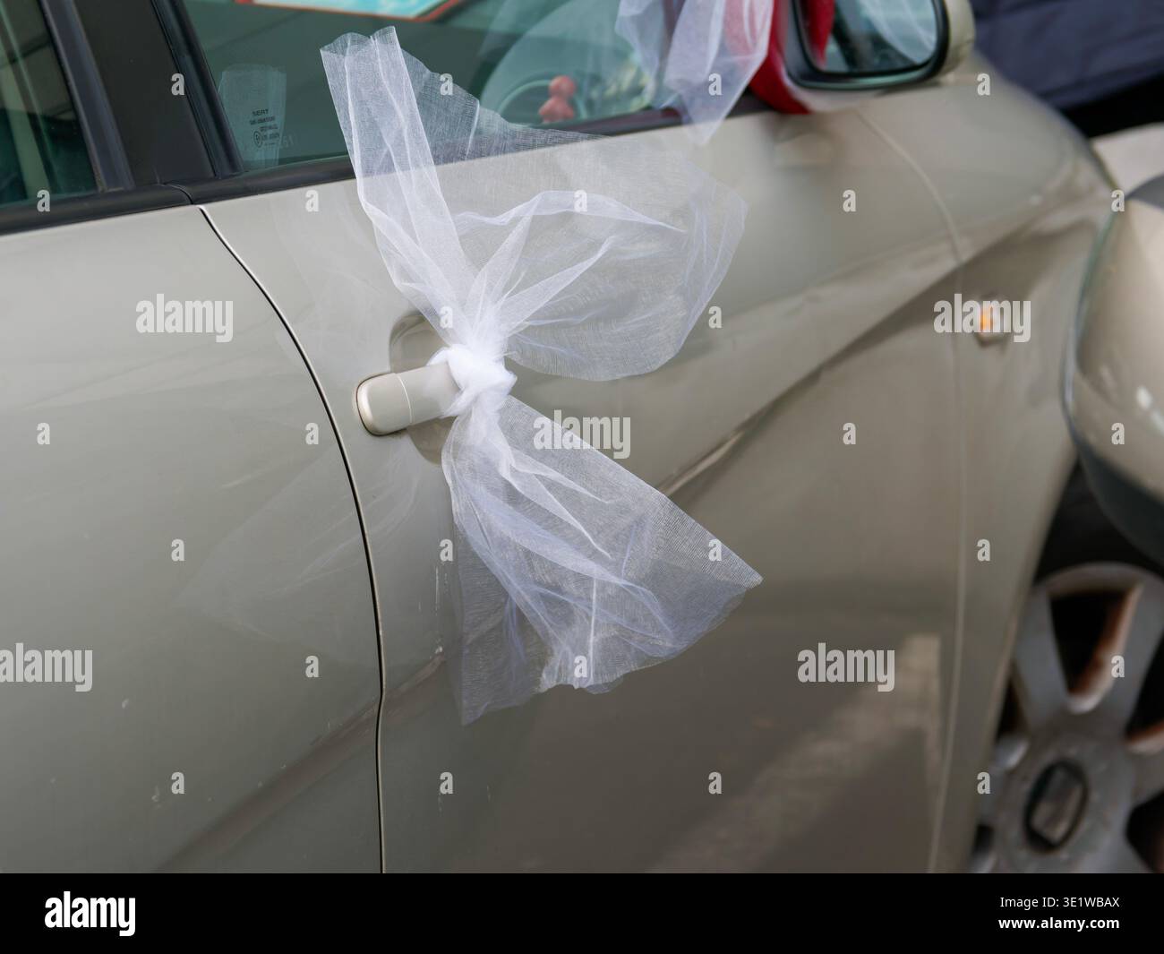 Primo piano di un'auto per matrimoni decorata con un nastro di tulle bianco legato alla maniglia della portiera, simboleggia una celebrazione del matrimonio e un'occasione festiva. Foto Stock