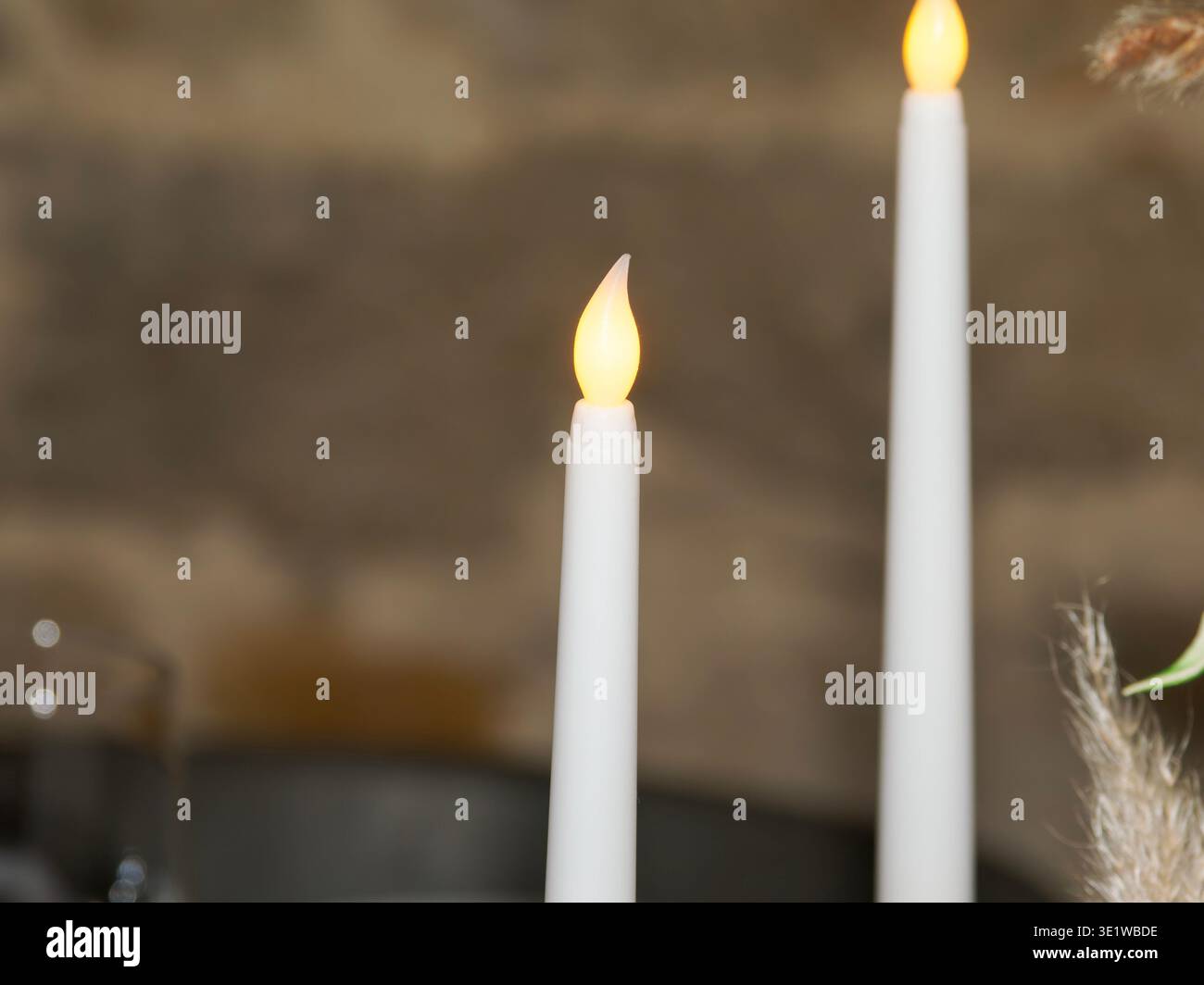 Primo piano di due candele bianche accese che creano un'atmosfera calda e intima, una luce soffusa e uno sfondo sfocato per un ambiente accogliente ed elegante Foto Stock