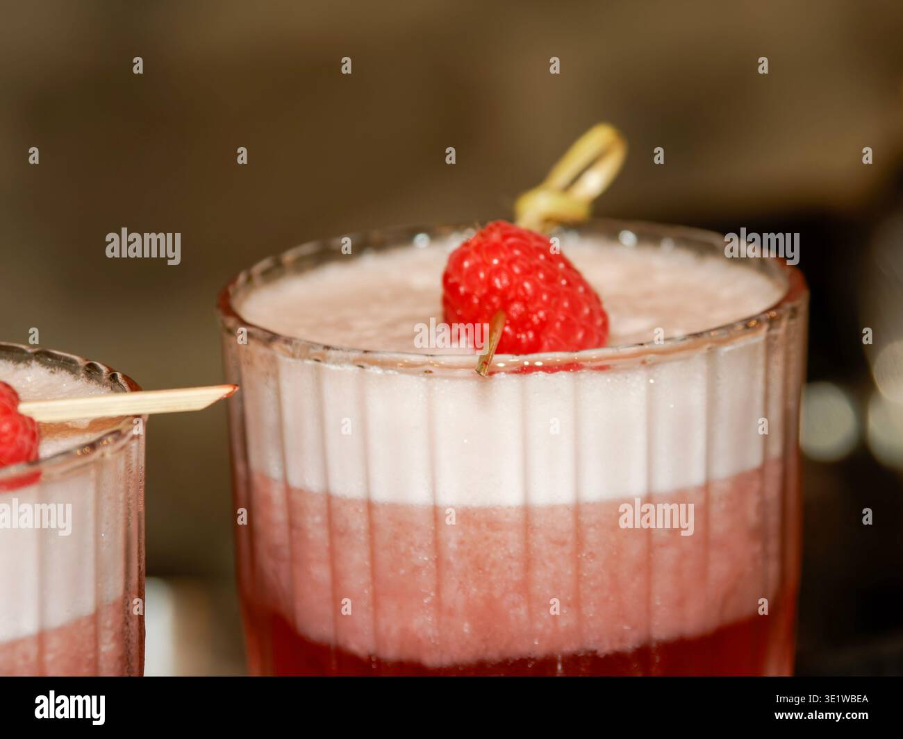 Primo piano di un elegante dessert al lampone servito in un bicchiere, caratterizzato da una crema di mousse bianca e strati di frutta rossa conditi con un lampone fresco. Foto Stock