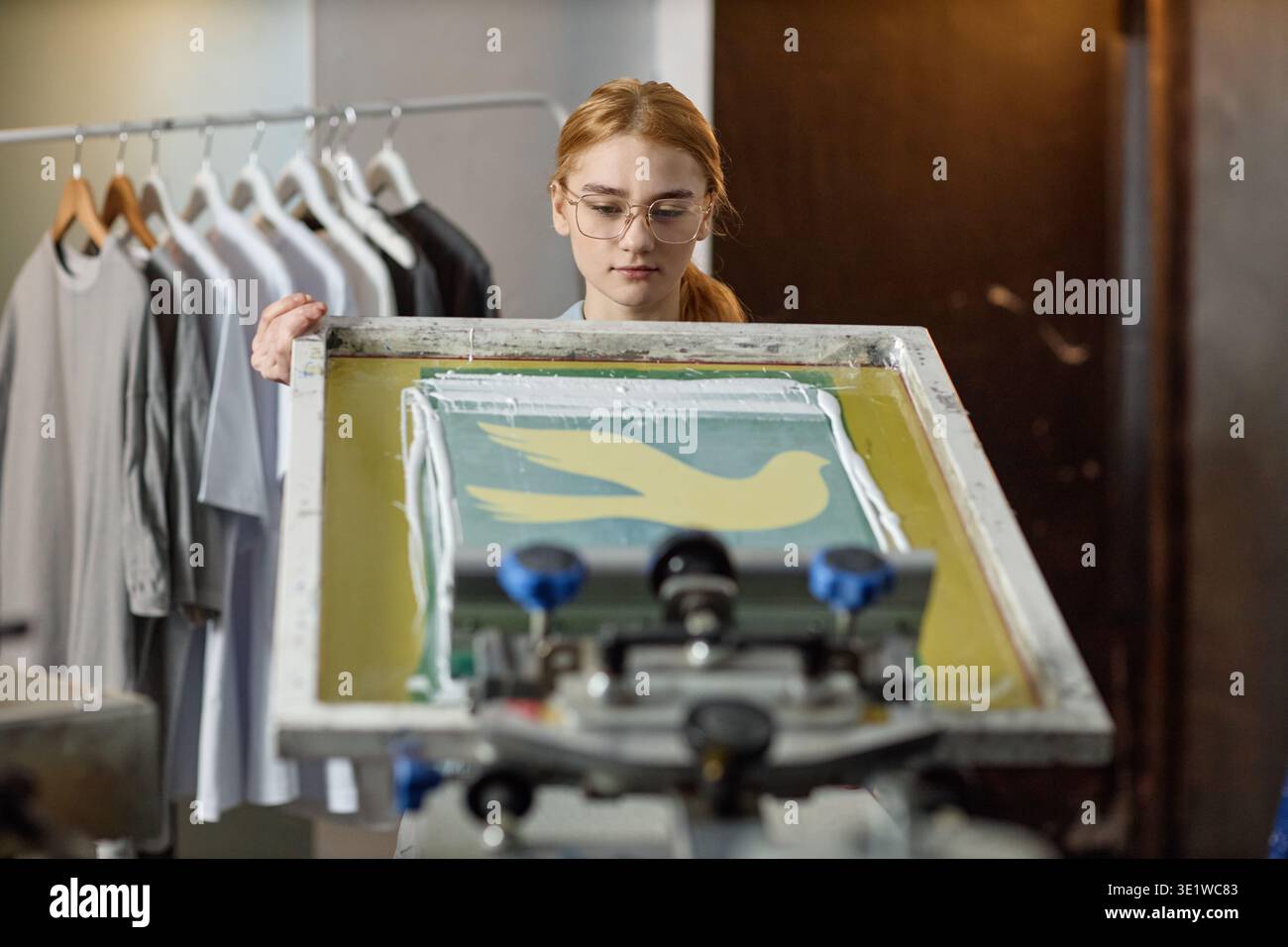 Young Woman Screen Printing Bird Design su tessuto in officina Foto Stock