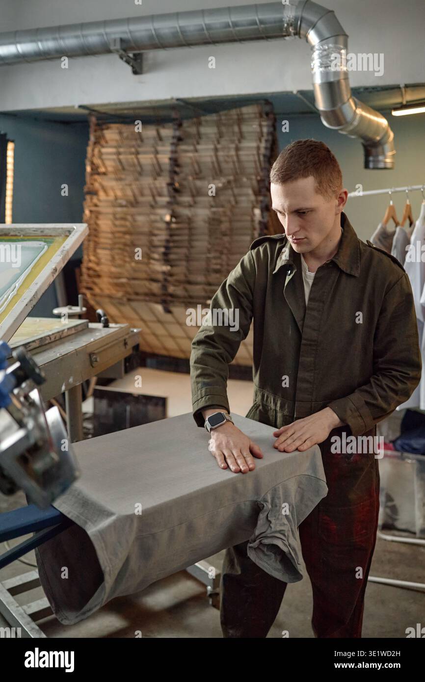 Verticale di Young Man preparazione tessuto su macchina da stampa su schermo in officina Foto Stock
