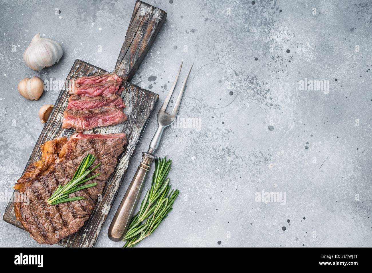 Bistecca newyorkese stagionata a secco, grigliata alla perfezione con erbe e aglio su una superficie grigia ruvida per concetti culinari Foto Stock