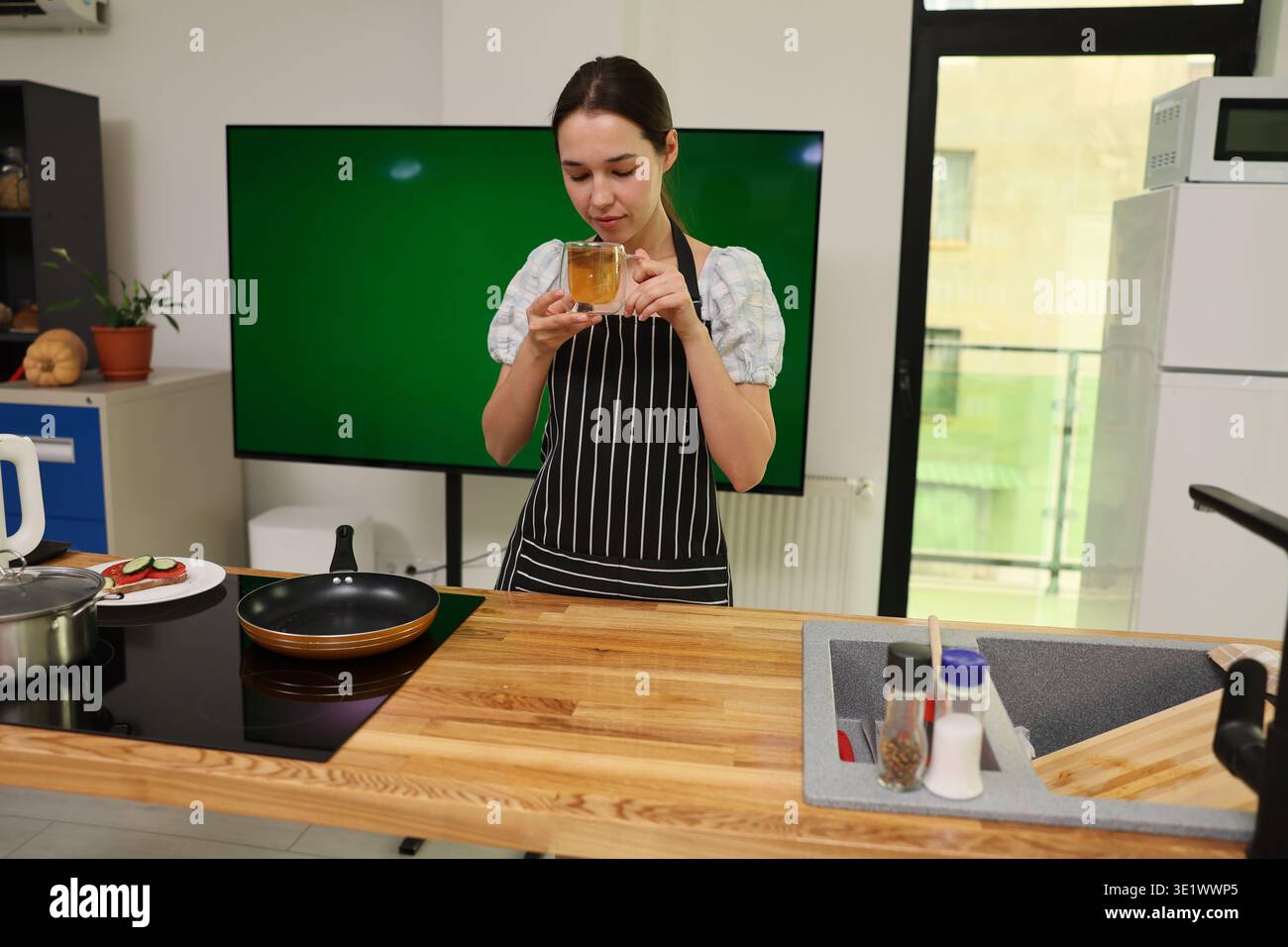 La giovane donna in cucina moderna crea una bevanda rinfrescante mentre prepara un pasto con cura e creatività Foto Stock