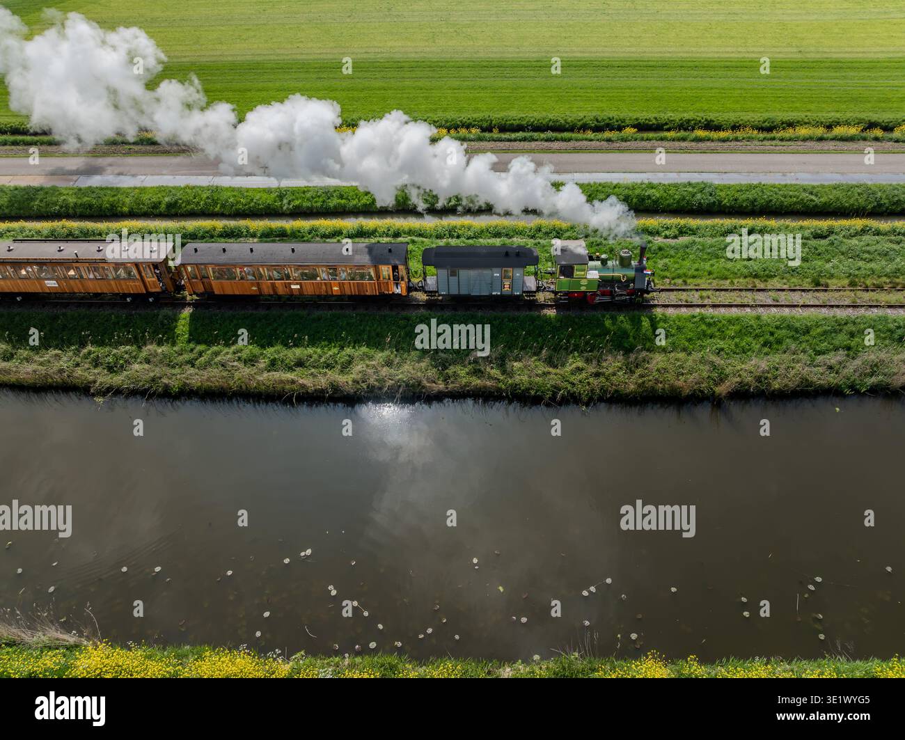 Veduta aerea di un treno a vapore d'epoca lungo i binari, in contrasto con i campi verdi luminosi e un canale scuro, Benningbroek, Noord-Holland, N Foto Stock