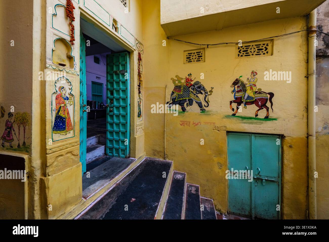 I tradizionali dipinti murali Rajasthani di un elefante e un cavaliere decorano l'ingresso giallo di un edificio vicino al Palazzo della città di Udaipur. Udaipu Foto Stock