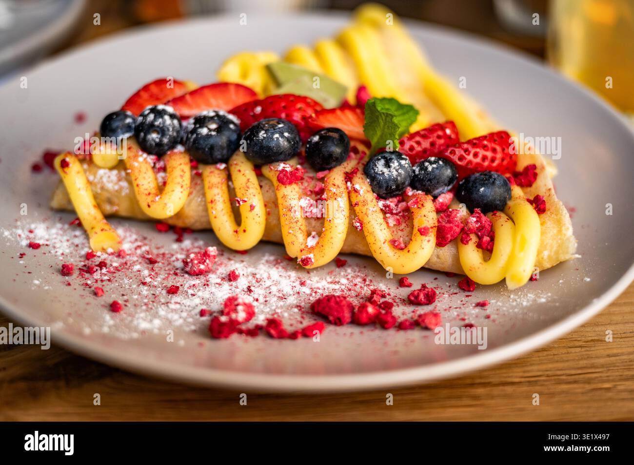 Pancake con mirtilli e fragole a fette decorato con crema di vaniglia su piatto grigio. Foto Stock
