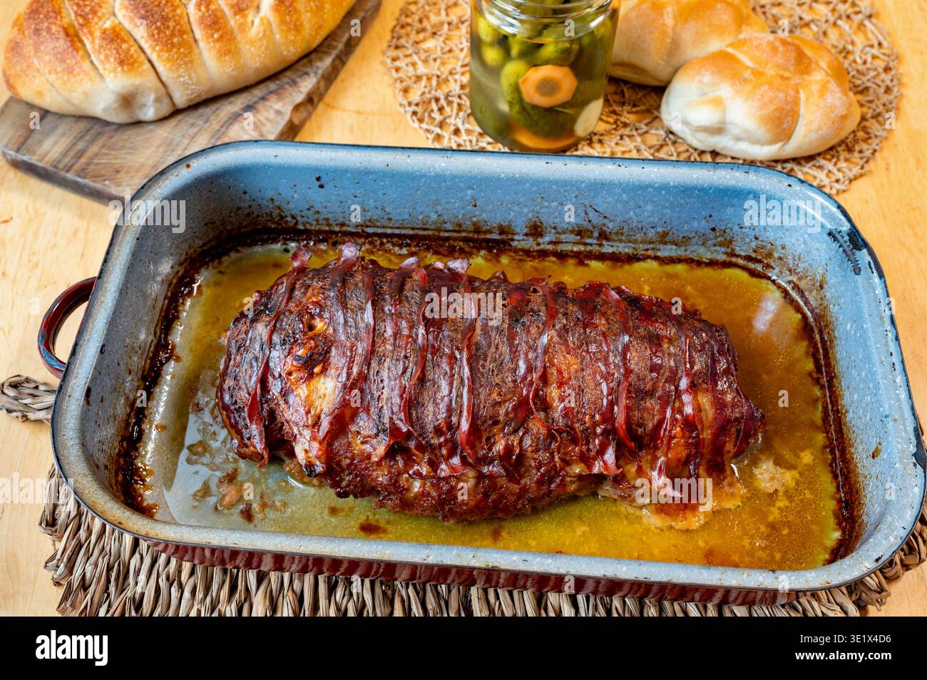Pane di carne macinata al forno con pancetta nella vecchia padella, panino fresco e cetriolo sottaceto sul tavolo. Foto Stock