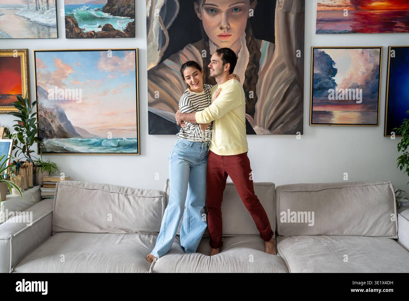 Felice coppia sposata di pittori uomo e donna che abbracciano sul divano di fronte alla mostra della galleria Home. Foto Stock