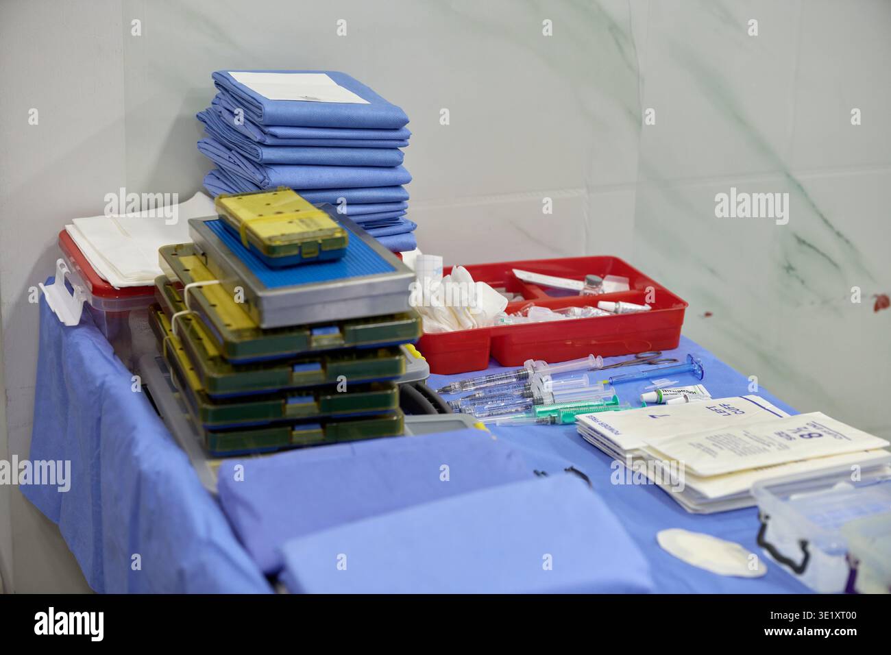 Piano di preparazione della sala operatoria con vassoi per strumenti sterili impilati, siringhe, fiale, garza, teli e materiale di consumo medico su coperchio sterile blu. Foto Stock