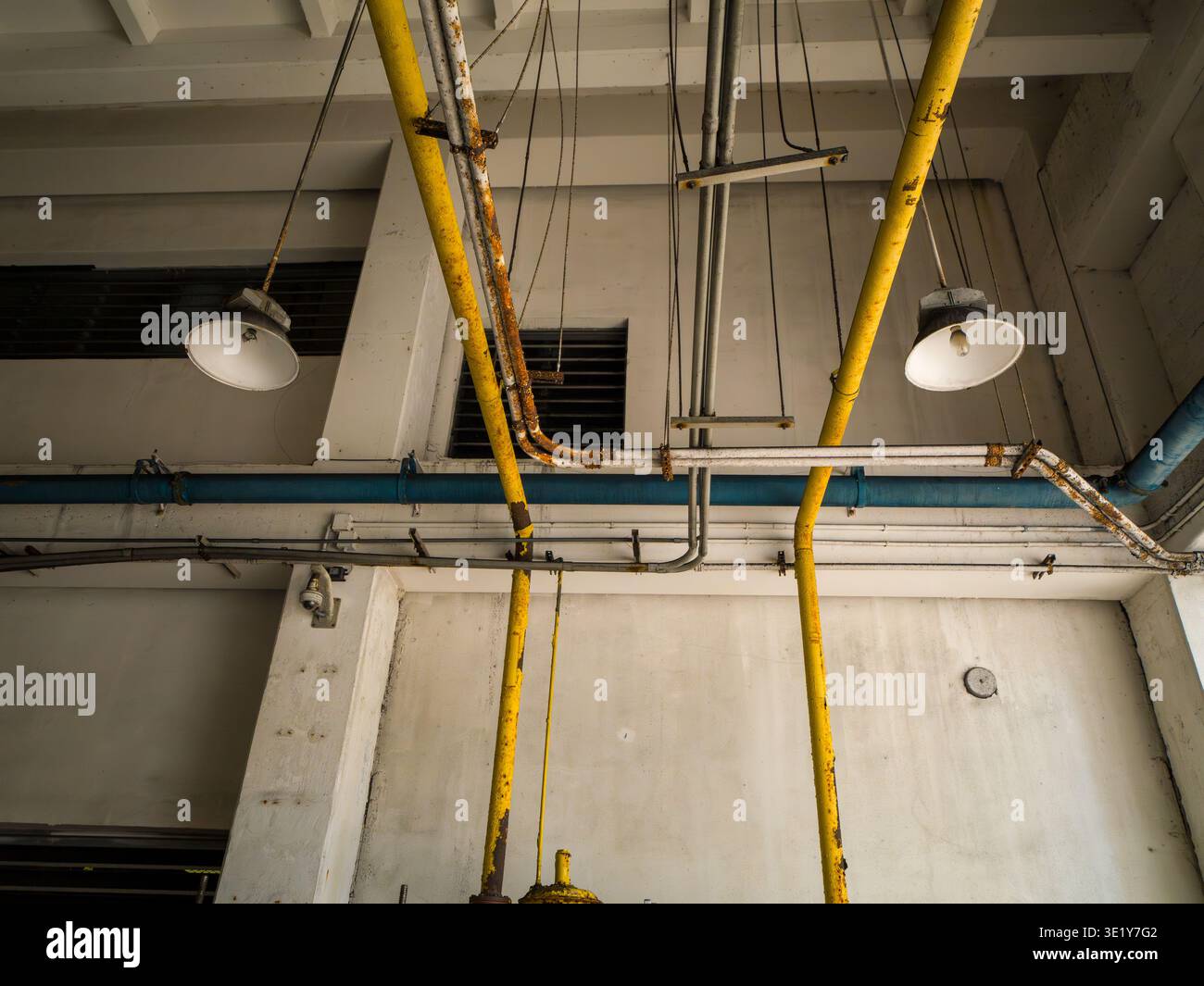 Ripresa ad angolo basso di un soffitto bianco in una stanza di servizio con impianti di illuminazione industriali e una rete di tubi gialli e blu. Foto Stock