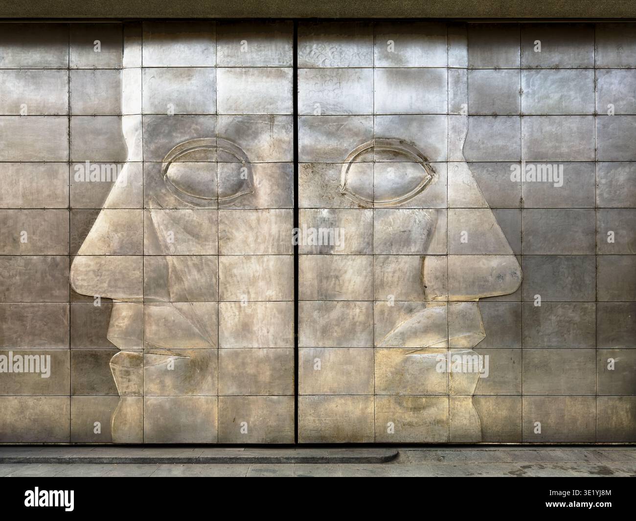 Due facce guardano in direzioni opposte sulle porte metalliche esterne del garage di carico di una sala espositiva a Praga. Foto Stock