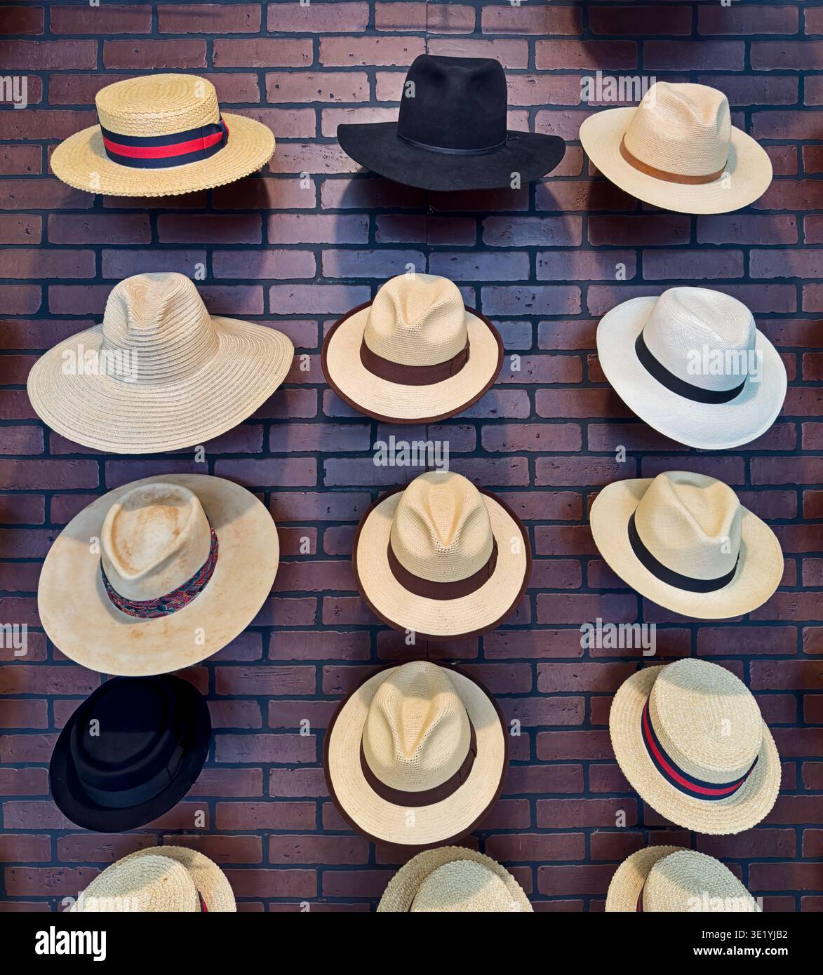 Un'esposizione di cappelli fatti su misura contro un muro con tredici cappelli di paglia Panama bianca e due cappelli neri. Foto Stock