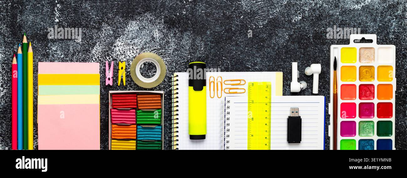 Striscione colorato Back to School con cancelleria, notebook, tavolozza di acquerelli, auricolari e unità flash su sfondo scuro con texture scure, stile creativo Foto Stock